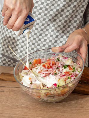 Ein Koch gie&szlig;t fettreduzierte Sahne in einen Salat