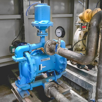 Blaue Elektrische Doppelmembranpumpe mit angeschlossenen Rohrleitung in einer industriellen Anlage f&uuml;r die Herstellung von Wellpappe.