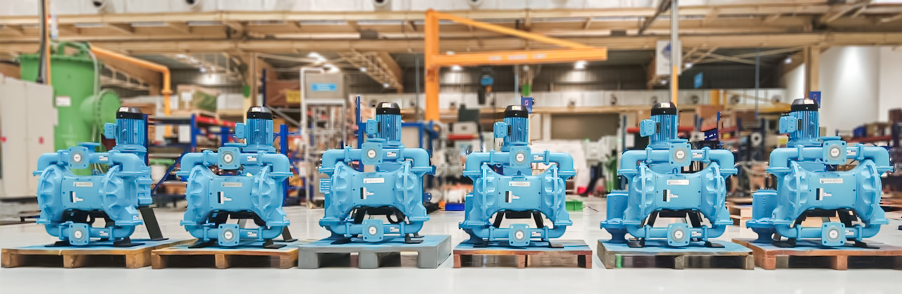 Lagerbestand an testpumpen der elektrischen Membranpumpe von Cognito Sechs blaue elektrische Membranpumpen sind in Reihe auf Paletten in einer Werkhalle aufgestellt.