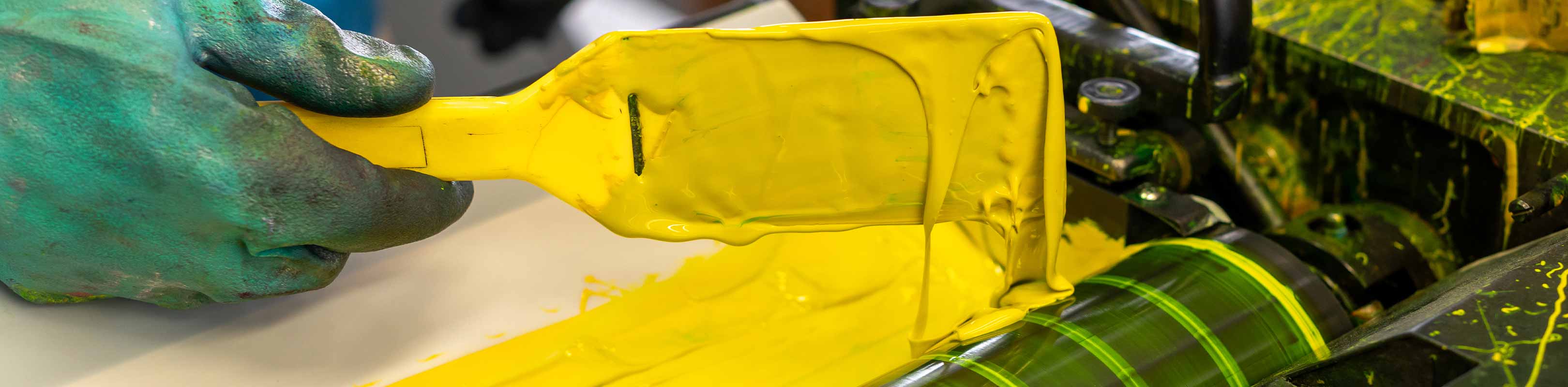Pinsel mit gelber Farbe tr&auml;gt die Farbe auf den Farbkasten einer Druckmaschine auf.