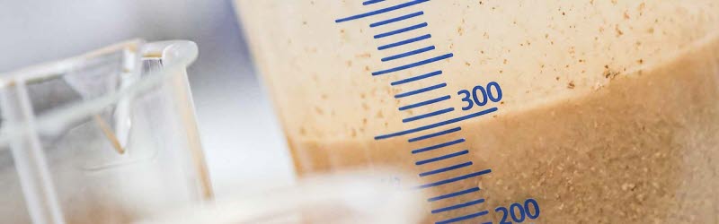 Leimhaltige Abwässer aus der Wellpappenindustrie Leimhaltiges Abwasser mit Schwebstoffen in einem Messbecher